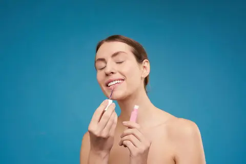 Woman applying lip gloss against blue background